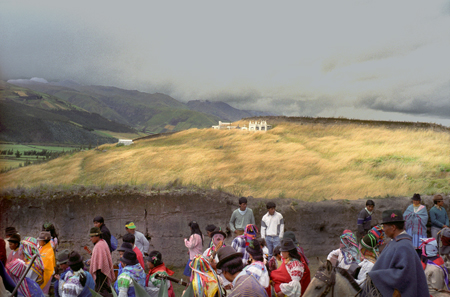 Color photograph by Barbara Beirne taken in the Ecuadorian Andes. A procession of indigenous people in traditional dress walk past at the bottom of the frame. A grassy hill is in the middle of the frame, and a valley and mountains can be seein in the background.